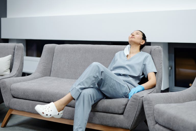 Nurse in scrubs takes a break, resting on a comfy hospital couch after a long shift.