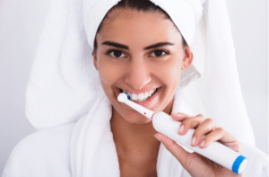Beautiful Woman In Bathrobe Brushing Teeth Using Electric Toothbrush