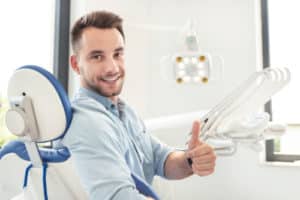Handsome man showing thumbs up and smiling sitting at the dental chair.