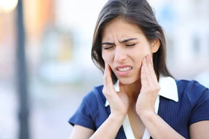 Woman rubbing her jaw in pain from her TMJ disorder.
