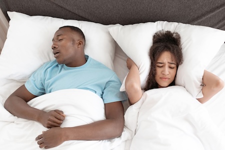 Apnea, freaking out, sufferers insomnia of snoring. Husband snores loudly and angry frustrated young african american wife can not sleep of noise, lady covers ears with pillow, top view, free space