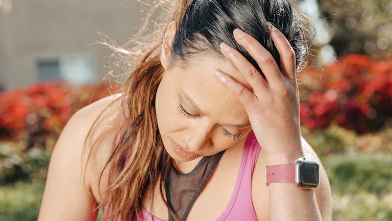 Close-up of a woman with a headache sitting outdoors wearing a smartwatch.