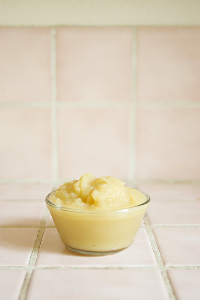 A minimalist food shot featuring mashed potatoes in a clear glass bowl against a tiled background.