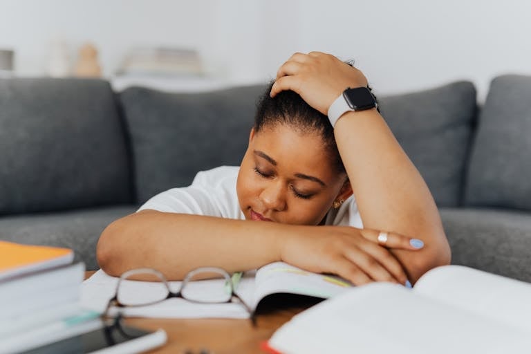 A woman rests on textbooks, exhausted from studying in her cozy living room environment.