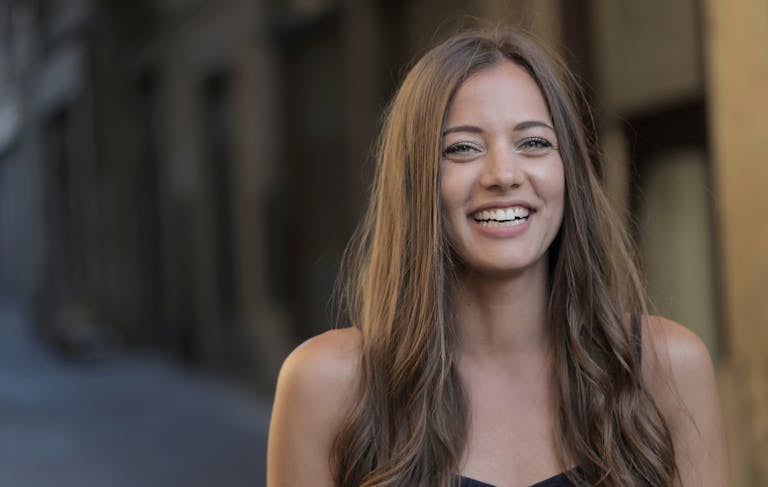 A woman with long hair smiling in an urban outdoor scene.