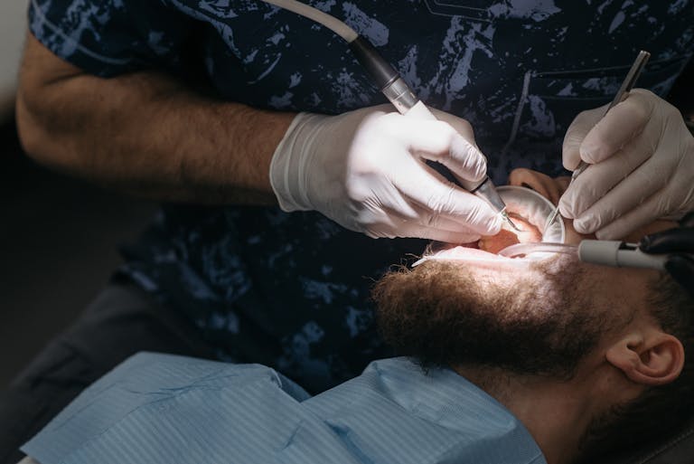 Dentist using tools for dental examination on a bearded male patient.