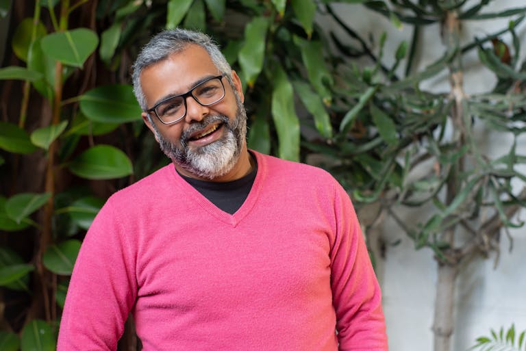 A joyful elderly man with glasses in a pink sweater enjoying the outdoors.